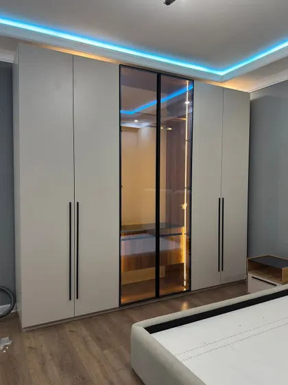 A beautiful wardrobe design with a central glass panel. The tinted glass and internal lighting create a stylish display for accessories, while the matte white shutters keep the look clean.