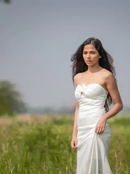 A beautiful shot of a model in a white dress walking through a field. This editorial portrait has a natural, windswept, and romantic feel.