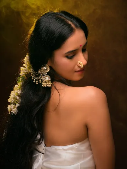 A classic ethnic portrait with a focus on traditional jewelry. The warm lighting and rich brown background create a painterly effect, emphasizing the model's serene beauty.