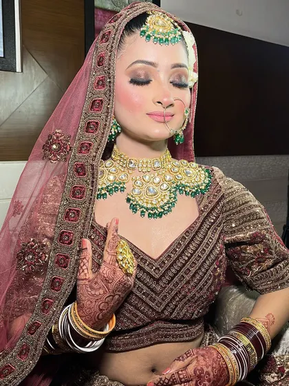A close-up of a bride in a similar wine-colored lehenga, this time paired with a stunning green kundan jewellery set.