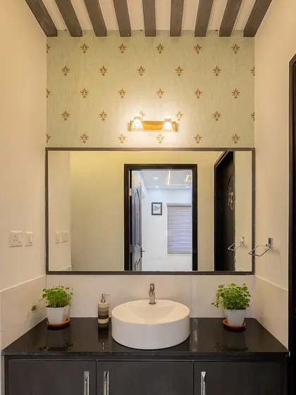 The powder room in the same Bangalore home features elegant wallpaper, a vessel sink, and plants, creating a welcoming space for guests.