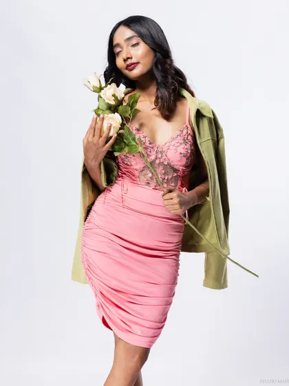 A model in a pink dress and green jacket, holding roses, for a stylish and layered look.