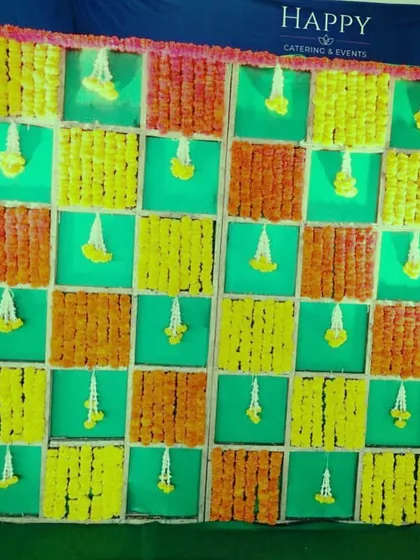 This bright and festive backdrop uses a checkerboard pattern of orange and yellow marigolds against green panels. The hanging jasmine buds add a touch of elegance to the vibrant design.