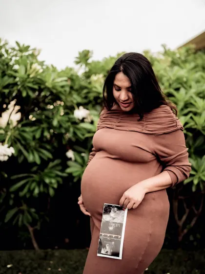 A serene portrait of the mom-to-be in a garden, looking down at the sonogram pictures held against her bump.