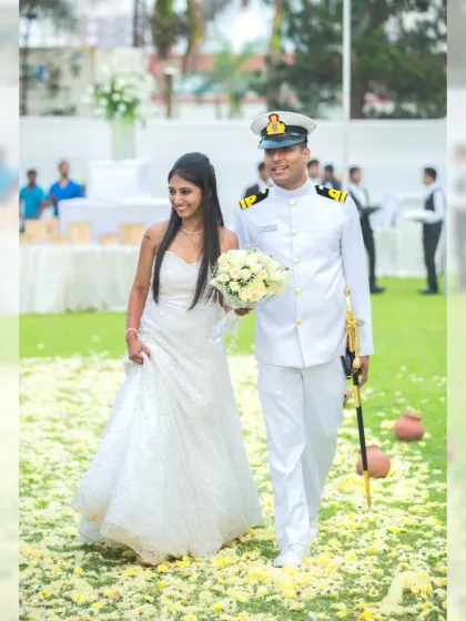The happy couple walks down an aisle of flower petals after their Christian wedding ceremony, the groom dressed in his handsome naval uniform.