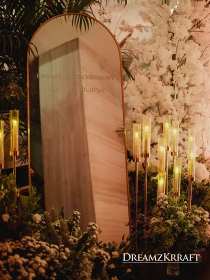 A modern and elegant welcome sign for the engagement ceremony, etched onto a marble-finish mirror. This piece is flanked by white florals and contemporary candle holders.