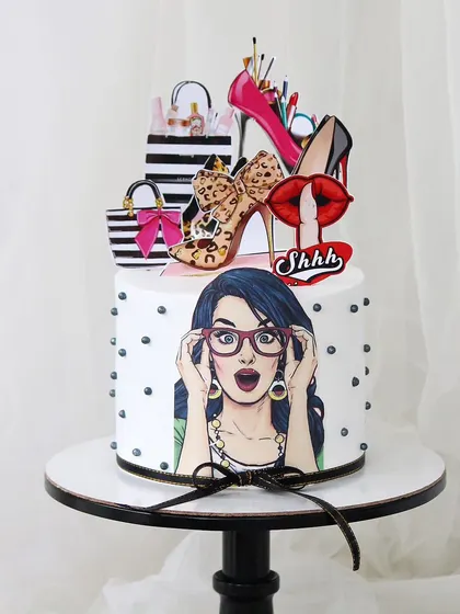 A quirky and fun pop-art-style cake for a diva. This design features a surprised woman graphic, topped with edible high heels, shopping bags, and lipstick for a playful and stylish celebration.