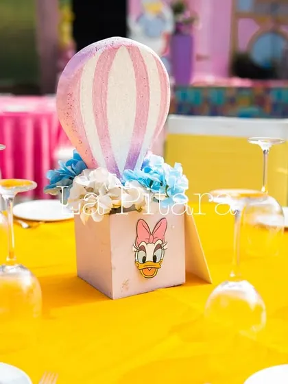 A close-up of a table centerpiece featuring a Daisy Duck-themed box with a miniature hot air balloon. These small, thoughtful details are what make a themed party truly special.