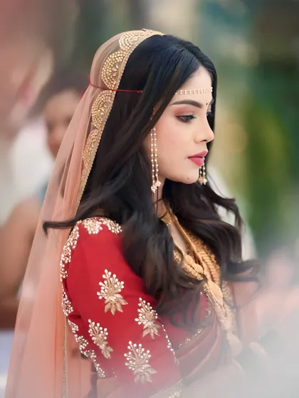 A stunning side profile of the bride. The focus is on her elegant makeup, with a sharp winged eyeliner and bold red lip, and her unique headband-style 'mundavalya'.