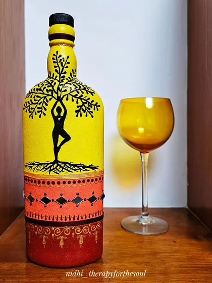 A decorative bottle painted with a yoga tree-pose silhouette against a bright yellow background. The base features traditional patterns and mirror work, blending modern themes with folk art.