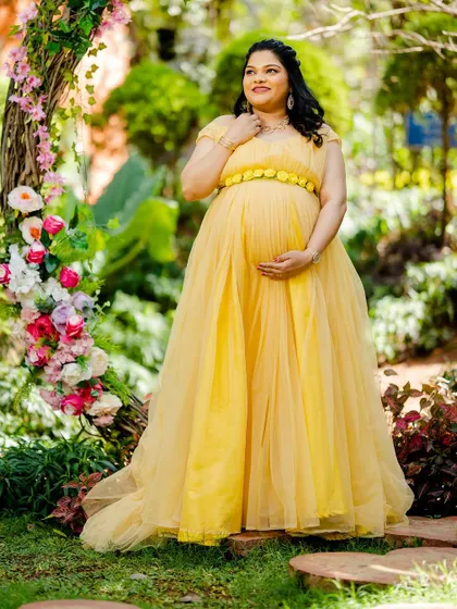 A radiant mom-to-be in a flowing yellow gown, framed by a rustic floral arch. The soft lighting and cheerful colors create a picture of pure happiness.