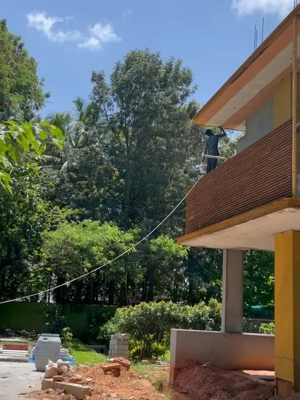 A park-facing home for an NRI client under construction, with workers applying finishes to the facade.