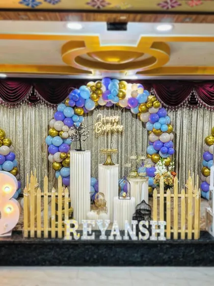 A birthday stage setup in a classic convention hall. I used a blue, purple, and gold balloon arch and a full set of props to create a grand focal point for the celebration.