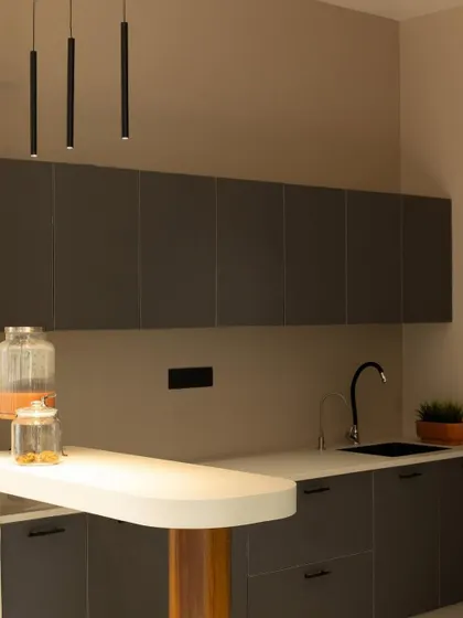 A clean shot of the office pantry, focusing on the minimalist grey cabinetry, black faucet, and sleek white countertop.