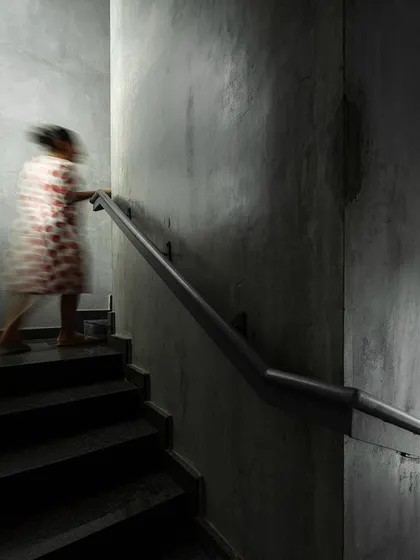 The main staircase is enclosed in raw concrete walls, with subtle lighting creating a moody and atmospheric passage. The motion-blurred figure suggests the constant movement and energy within the studio.