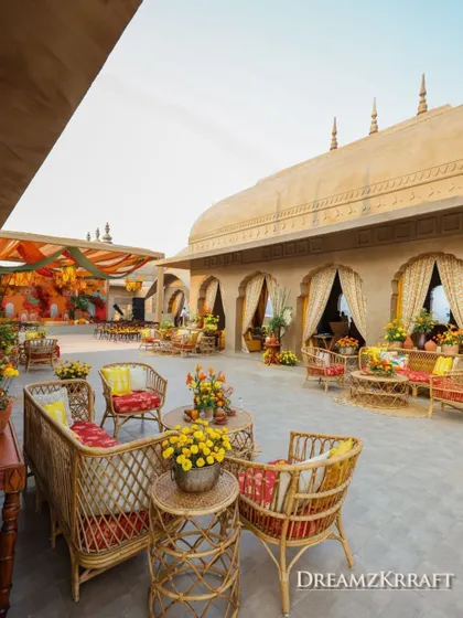 A beautiful courtyard setup for the Haldi, with rattan furniture and colorful cushions creating a relaxed and festive atmosphere against the palatial architecture.