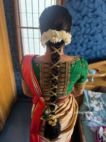 A unique take on the traditional braid, this style features a crisscross pattern using gold ribbon that complements the bride's green and gold Kanjeevaram saree. The braid is finished with jasmine flowers and a parandi.