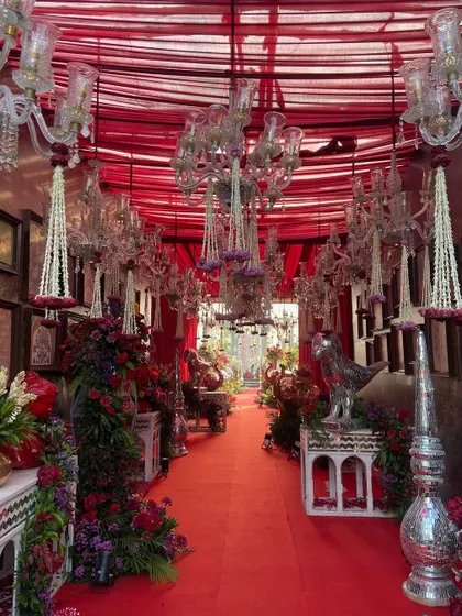 An immersive view of an indoor celebration space, drenched in red. The ceiling is draped with red fabric and hung with crystal chandeliers and floral tassels, leading guests down a path of pure opulence.