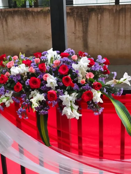 Railing decoration for a corporate event, featuring a lush floral arrangement of red, white, and purple flowers tied with a white sash.