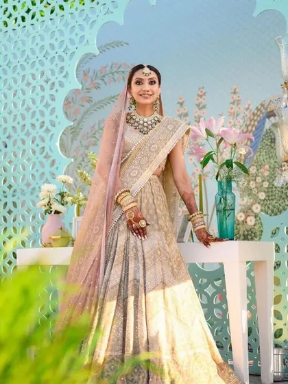 A beautiful bride in her pastel lehenga, posing against the elegant decor. The design features a custom jaali screen and a soft color palette that enhances her ethereal look.