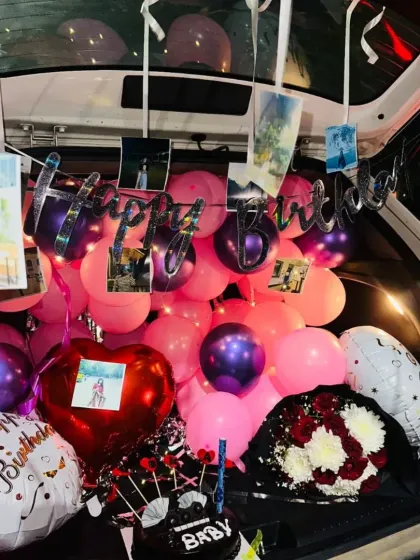 This car trunk decoration includes a "Happy Birthday Baby" cake, a flower bouquet, and a mix of foil and latex balloons.