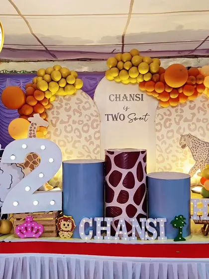 A complete jungle-themed stage for a second birthday. The setup includes a 'Two Sweet' backdrop, animal-print plinths, a large light-up number '2', and cutouts of a sheep and giraffe.