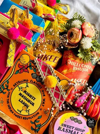 A flat lay of some of the colorful items from our Holi hampers, including Mighty Motichur Laddu and Chilli Cheese Bhujia.