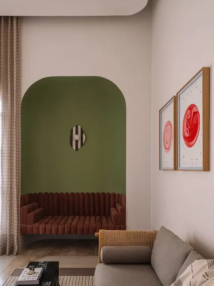 A cozy seating nook is recessed into an olive-green arched wall, creating an intimate spot within the larger home office. The fluted sofa in a rust color adds texture and warmth.