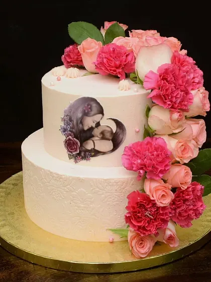 I made this special two-tier cake for a new mom's birthday. It features an edible print of a mother and child, surrounded by a cascade of fresh pink roses and carnations for an elegant and heartfelt celebration.