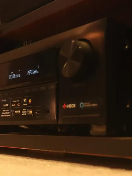 A close-up of a Denon AV receiver, the central hub that powers the speakers and connects all the video sources in this 7.1.2 home cinema.