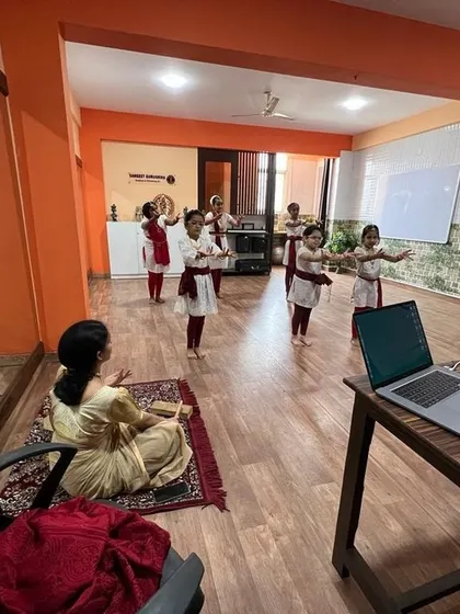 A Bharatanatyam practical exam in progress, with an instructor seated and observing the students' performance.