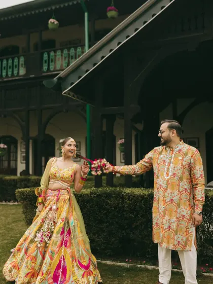A fun and playful shot of the couple. The bride's colorful lehenga and the groom's printed kurta are perfect for their outdoor Haldi carnival.