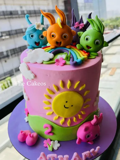 A bright and cheerful cake featuring the characters from Sunny Bunnies. This pink cake is decorated with a smiling sun, a rainbow, and all five colorful bunny characters made from fondant.