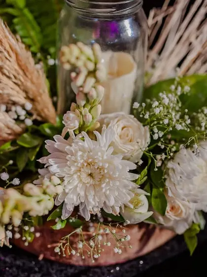 A rustic table centerpiece featuring white chrysanthemums, pampas grass, and a candle in a jar, perfect for a nature-inspired theme.