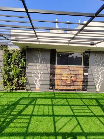 A frontal view of the feature wall, with the Buddha art centered between two vertical gardens and two backlit tree sculptures, under a modern pergola.