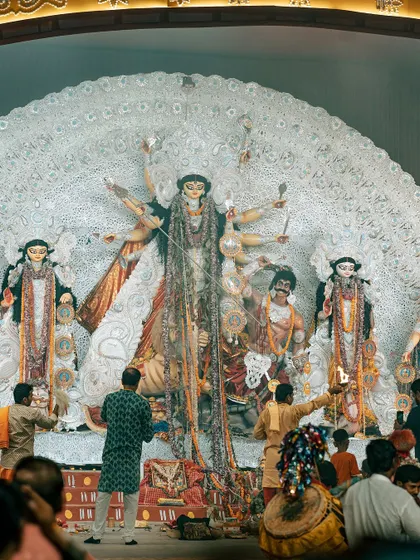 A wide shot of the Durga Puja pandal, showing the priests performing the aarti in front of a beautifully crafted idol made of sustainable materials.