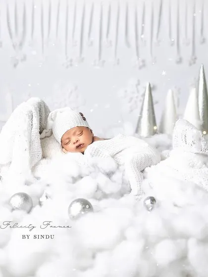 A perfect little snowflake dreaming in a winter wonderland. This all-white setup with soft cotton clouds and twinkling lights creates a magical, serene atmosphere for a newborn photoshoot.