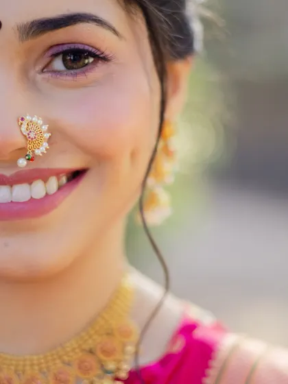A smile that lights up the room. This extreme close-up focuses on the flawless makeup application, the beautiful smile, and the traditional peacock-design nath.
