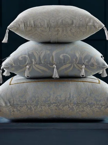 A stack of three elegant cushions with tassels, shot against a dark, moody background. This clean and simple composition focuses all attention on the product details and luxurious fabric.