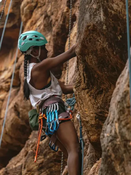 A climber, fully kitted out with gear on her harness, ascends a rock face. Our rope climbing sessions teach you how to manage your gear and climb efficiently.