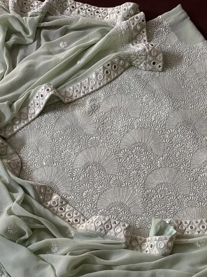 Experience modern elegance with our Mint Green suit in pure georgette. The fabric is adorned with a heavy 'Teen Taar' Chikankari jaal, which is further illuminated by Poth, Kutdana, and a handcrafted Kutchi mirrorwork border for a touch of refined glamour.