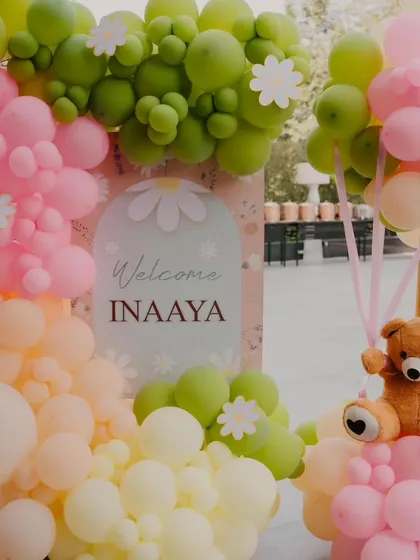 A close-up of the welcome sign and balloon details for Inaaya's party, featuring a soft, gentle color scheme.