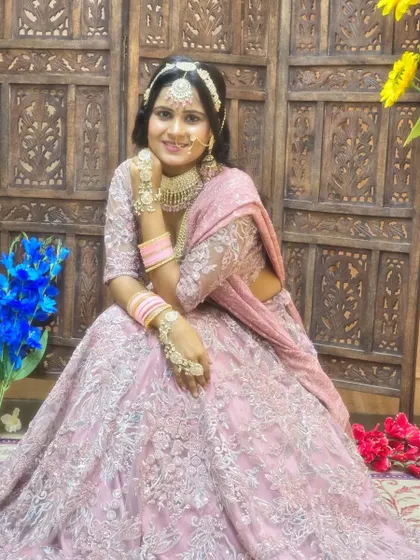 A soft and pretty bridal look. The jewellery set with a delicate choker, maang tikka, and haath phool is customized with pink accents to match the pink lehenga.