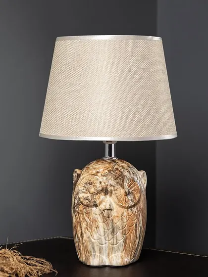 The Owl Wisdom table lamp features a ceramic base shaped like an owl with a rustic, wood-like finish. It's a unique and charming piece that adds a touch of nature-inspired wisdom to your room.