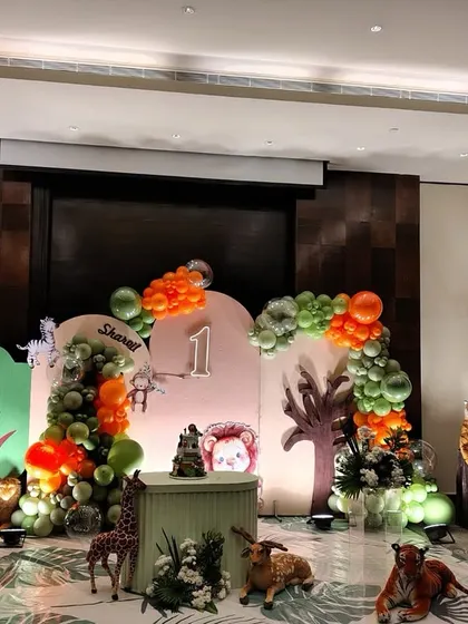 A wide view of our jungle safari theme, showcasing the full scope of the decoration. You can see the arrangement of life-sized animal props, the detailed balloon arches, and the central cake table, all working together to create a complete jungle environment in an indoor banquet hall.