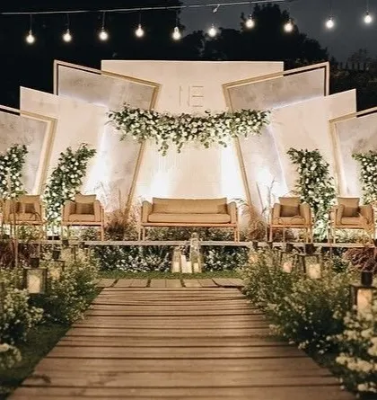 A rustic-modern reception stage with a geometric white backdrop, wooden aisle, and soft floral accents.