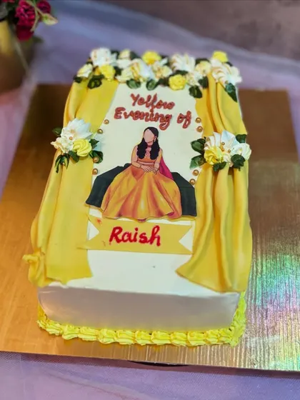 A personalized cake for a "Yellow Evening" or Haldi ceremony, featuring an edible print of the bride-to-be in her traditional attire, framed by yellow fondant curtains.