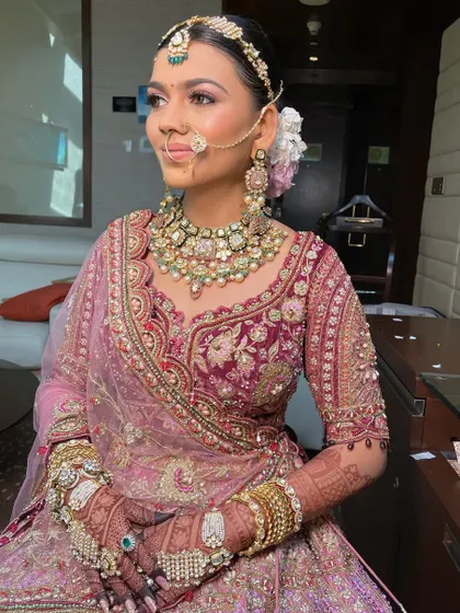 A royal bride in a deep pink lehenga. Her hair is styled in a classic updo, adorned with flowers, to match her majestic outfit.