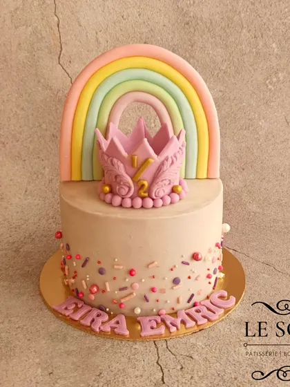 Celebrating a half-birthday with this adorable rainbow and crown cake. This half-kg Chocolate Butterscotch cake features a pastel fondant rainbow and a detailed pink crown for the six-month milestone.