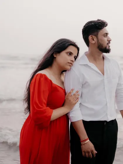 A quiet and contemplative portrait of a couple by the sea. She rests her head on his shoulder as they look out at the water, capturing a moment of peaceful togetherness.